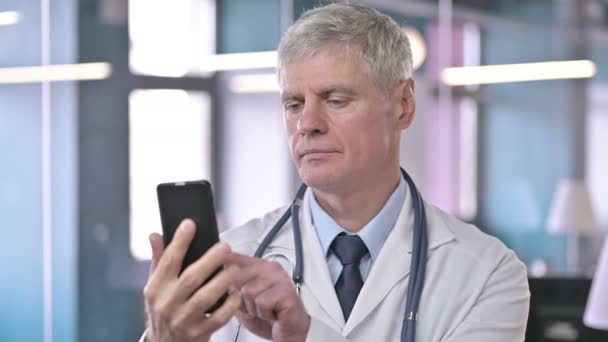 Porträt eines Arztes mittleren Alters, der auf dem Handy scrollt — Stockvideo