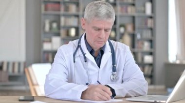 Ofiste otururken kağıtları yazan profesyonel kıdemli doktor.