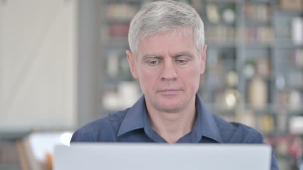 Retrato del hombre de mediana edad señalando con el dedo a la cámara y trabajando en el ordenador portátil — Vídeos de Stock