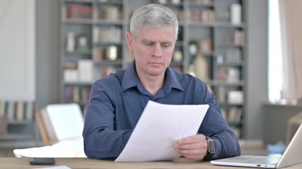 Hombre serio de mediana edad leyendo documentos mientras trabaja en la oficina — Vídeos de Stock