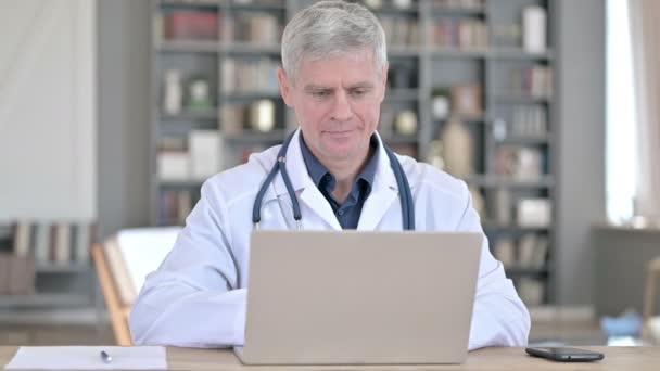 Профессиональный старший врач работает на ноутбуке во время работы в офисе — стоковое видео