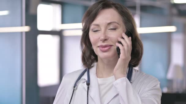 Портрет профессионального врача средних лет, улыбающегося и говорящего на смартфоне — стоковое видео