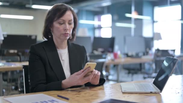 Χαρούμενη μεσήλικη επιχειρηματίας που χρησιμοποιεί Smartphone στο γραφείο — Αρχείο Βίντεο