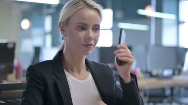 Молодая предпринимательница разговаривает по смартфону на работе — стоковое видео