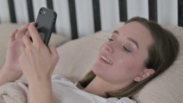 Vrolijke jonge vrouw met behulp van Smartphone in bed — Stockvideo