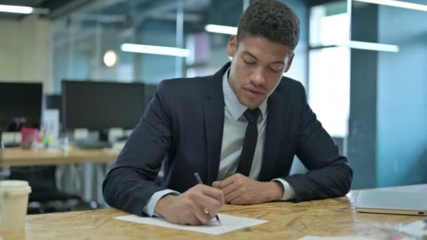 Молодий африканський бізнесмен пише на папері на службовому папері — стокове відео