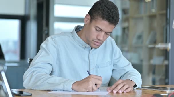 Ambitieuze Afrikaanse man die op papier schrijft met pen — Stockvideo