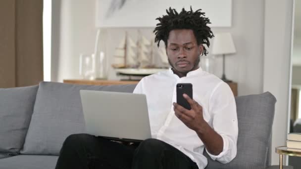 Hombre africano usando el ordenador portátil y el teléfono inteligente en el hogar — Vídeos de Stock