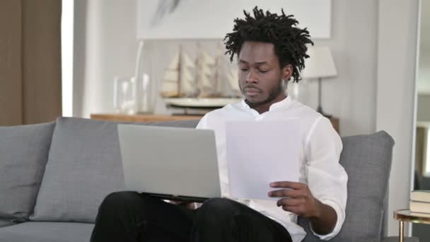 Afrikansk man som arbetar med dokument och bärbar dator hemma — Stockvideo