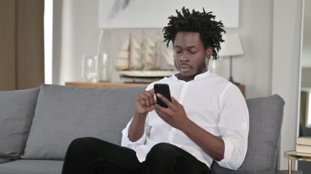 Spännande afrikanska mannen att ha framgång på smartphone hemma — Stockvideo