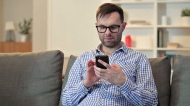 Ciddi genç adam evde akıllı telefon kullanıyor. 
