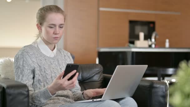 Jonge vrouw werkt op laptop en smartphone thuis — Stockvideo