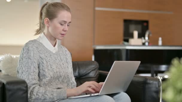 Jonge vrouw zit op de bank en werkt op laptop — Stockvideo