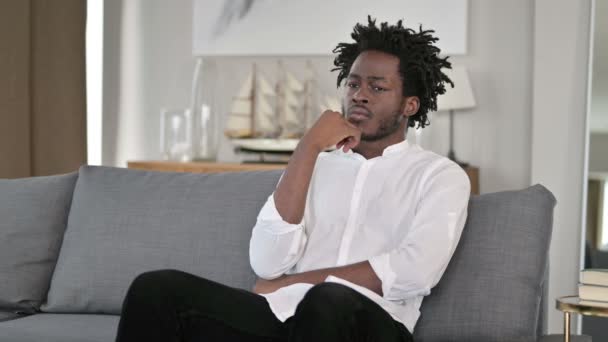 Młody Afrykanin siedzi w domu i myśli — Wideo stockowe