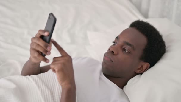 Αφρικανικός άνθρωπος που χρησιμοποιεί Smartphone στο κρεβάτι — Αρχείο Βίντεο