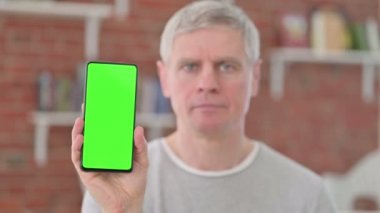 Yaşlı adam elinde krom ekranlı akıllı telefon tutuyor. 