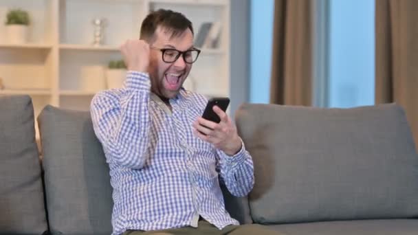 Hombre emocionado celebrando el éxito en el teléfono inteligente en casa — Vídeo de stock