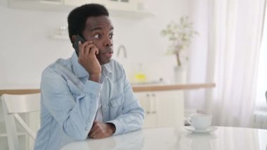 Evde akıllı telefondan konuşan neşeli Afrikalı adam.