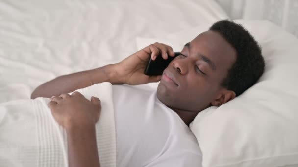 ベッドの中でスマートフォンで話す深刻なアフリカ人男性 — ストック動画