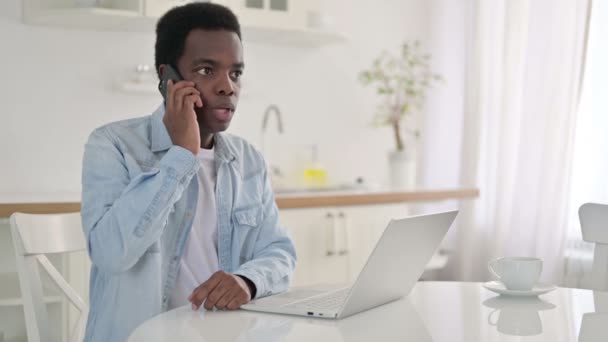 African Man z laptopem Mówienie na smartfonie w domu — Wideo stockowe