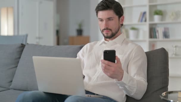 Зосереджений Бізнесмен працює над смартфоном і ноутбуком вдома — стокове відео