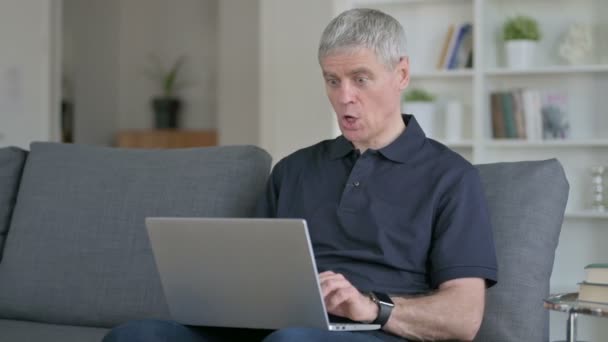 Överraskad medelålders affärsman som har framgång på laptop på soffan — Stockvideo