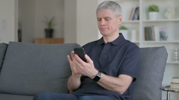 Empresário de meia-idade comemorando o sucesso no smartphone no sofá — Vídeo de Stock
