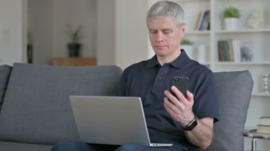 Akıllı telefon ve dizüstü bilgisayar kullanan çalışkan orta yaşlı iş adamı 