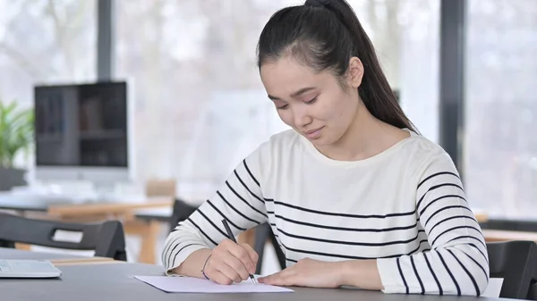 Young Asian Woman Writing in Office