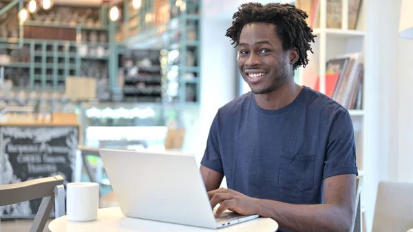 Afrikansk man med bärbar dator ler mot kameran i Café — Stockfoto