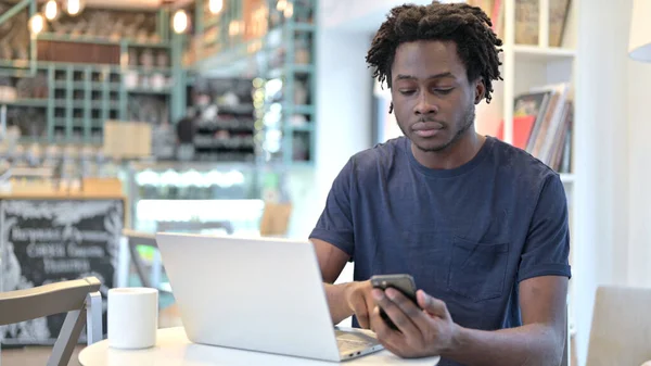 Afričan pomocí Smartphone a notebook v kavárně — Stock fotografie