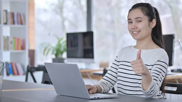 Pouces levées par la jeune femme asiatique en utilisant un ordinateur portable au bureau — Photo