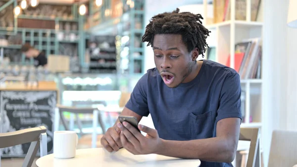 Africký muž slaví úspěch na Smartphone v Cafe — Stock fotografie