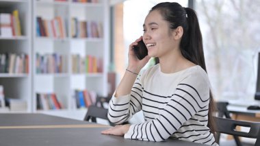 Güzel Asyalı Kadın Kütüphanede Akıllı Telefonla Konuşuyor