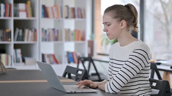 Jonge vrouw leest op laptop in de bibliotheek — Stockfoto