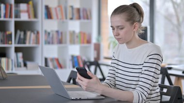 Kütüphanede Dizüstü bilgisayarlı Genç Kadın 'ın akıllı telefon kullanımı