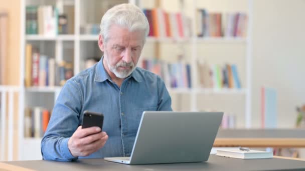 Anciano Senior Profesional usando Smartphone y Laptop en la Biblioteca — Vídeos de Stock