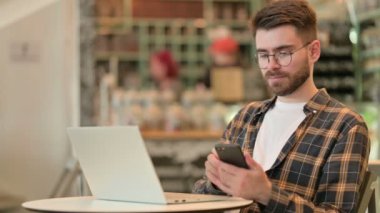 Laptop 'u olan genç adam Kafe' de Smartphone 'da konuşuyor. 