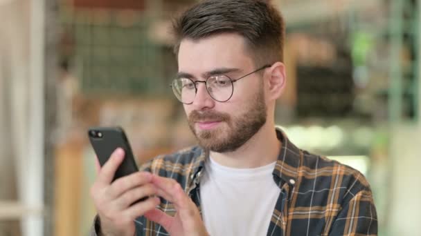 Dühös fiatalember portréja, aki okostelefonon vitatkozik. — Stock videók
