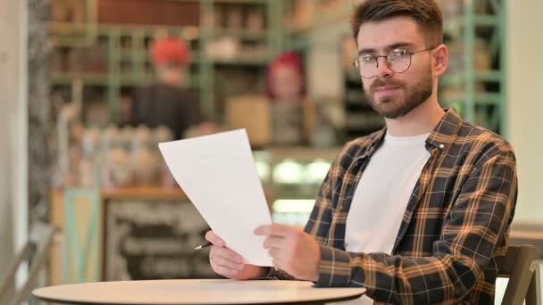 Mladý muž drží dokumenty a myšlení v kavárně — Stock video