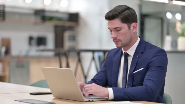 Серьезный бизнесмен с ноутбуком смотрит в камеру в офисе — стоковое видео