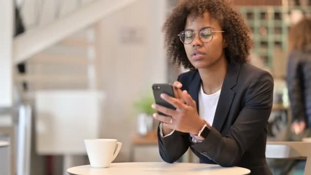 Mujer de negocios africana molesto reaccionar a la pérdida en el teléfono inteligente en Café — Vídeos de Stock