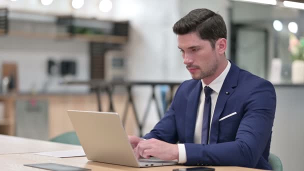 Веселый бизнесмен с ноутбуком улыбается в камеру в офисе — стоковое видео