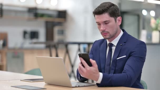 Бизнесмен с помощью смартфона и ноутбука в офисе — стоковое видео
