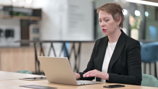 Oude zakenvrouw met laptop met rugpijn in kantoor — Stockvideo