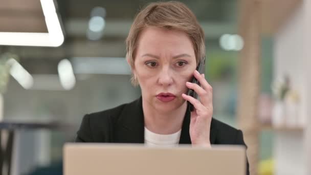 Κοντινό πλάνο του Old Businesswoman με Laptop Μιλώντας στο Smartphone — Αρχείο Βίντεο