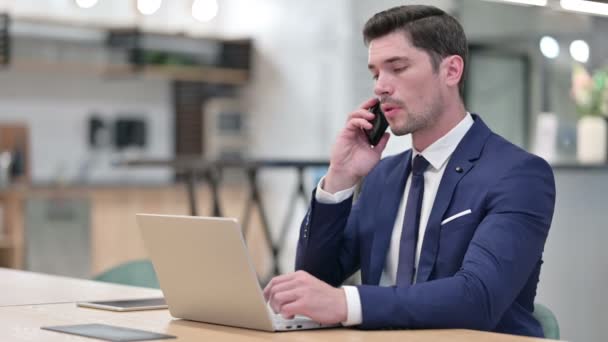 Biznesmen z laptopem Mówienie na smartfonie w biurze — Wideo stockowe