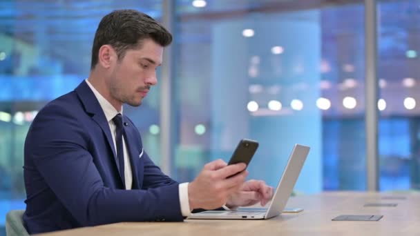 Uomo d'affari che utilizza smartphone e laptop al lavoro — Video Stock