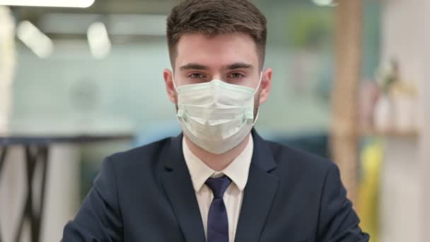 Молодой бизнесмен в защитной маске для лица показывает пальчики вверх — стоковое видео