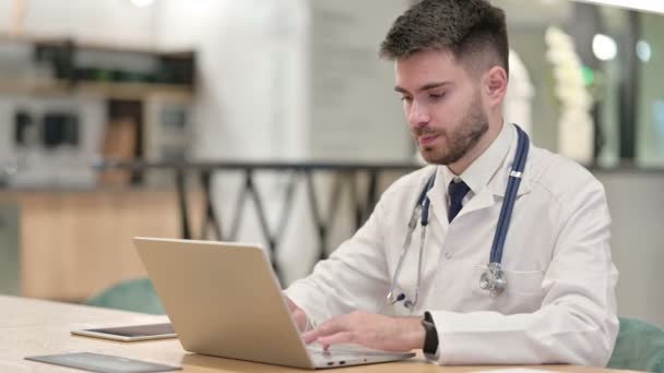 Młody lekarz z laptopem uśmiechnięty do kamery w biurze — Wideo stockowe